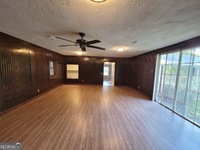 unfurnished living room featuring plenty of natural light, wood-type flooring, wood walls, and ceiling fan