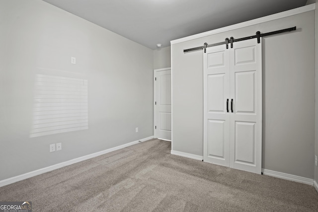 unfurnished bedroom with a barn door, baseboards, a closet, and carpet flooring