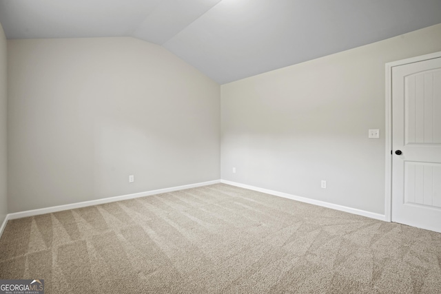 carpeted spare room featuring baseboards and vaulted ceiling