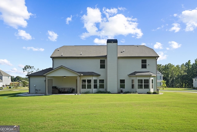 rear view of property featuring a shingled roof, a chimney, a yard, a patio area, and a ceiling fan