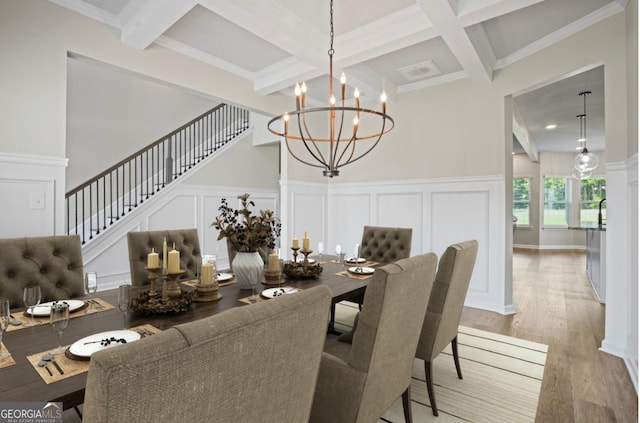 dining space with stairway, beam ceiling, an inviting chandelier, light wood-style floors, and a decorative wall