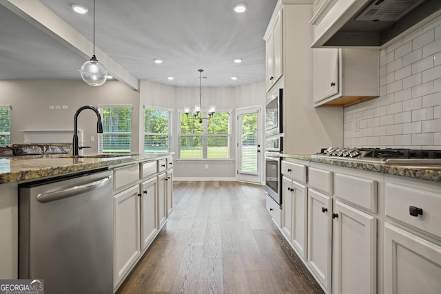 kitchen featuring backsplash, under cabinet range hood, dark stone counters, stainless steel appliances, and white cabinetry