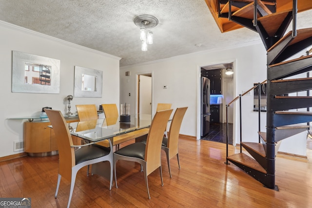 dining area with a textured ceiling, crown molding, and hardwood / wood-style flooring