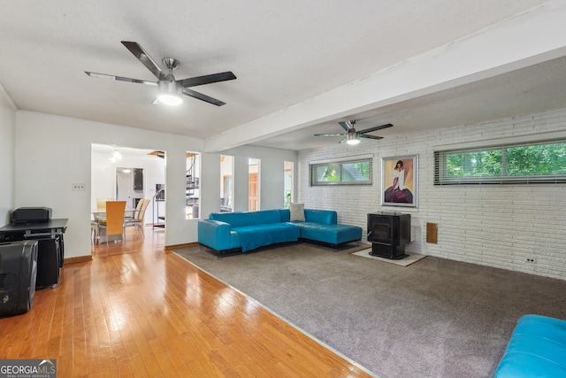 unfurnished living room with brick wall, a wood stove, beam ceiling, ceiling fan, and hardwood / wood-style floors