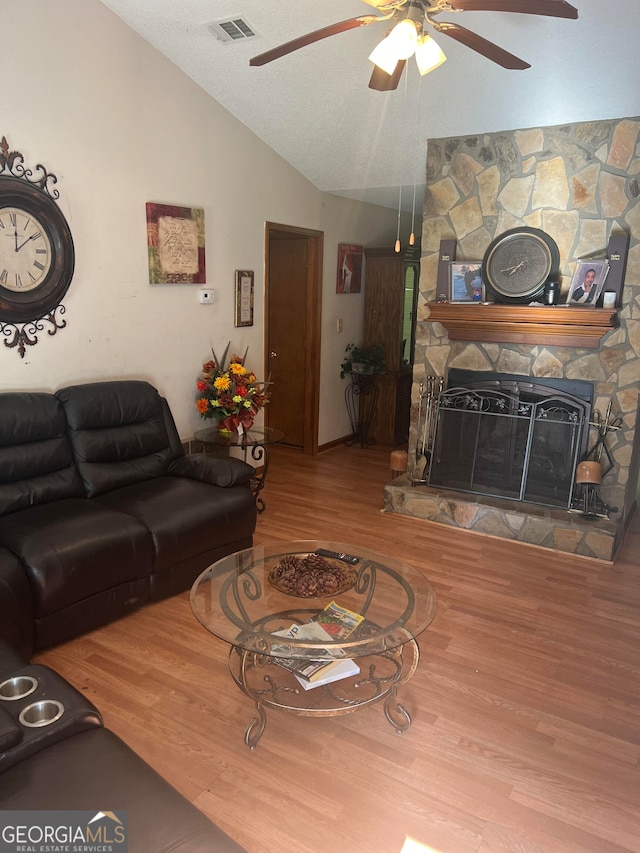 living room featuring ceiling fan, a stone fireplace, wood-type flooring, and vaulted ceiling