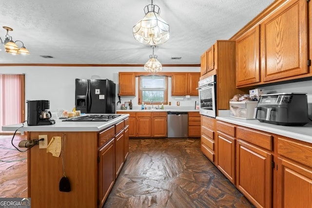 kitchen with a textured ceiling, a kitchen island, decorative light fixtures, a notable chandelier, and stainless steel appliances