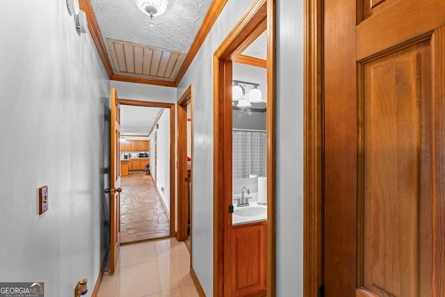 corridor featuring a textured ceiling, crown molding, sink, and light tile patterned floors