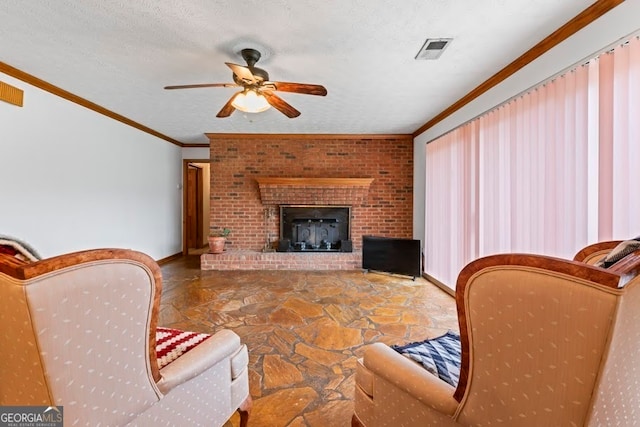 living room featuring ceiling fan, a brick fireplace, crown molding, and a textured ceiling