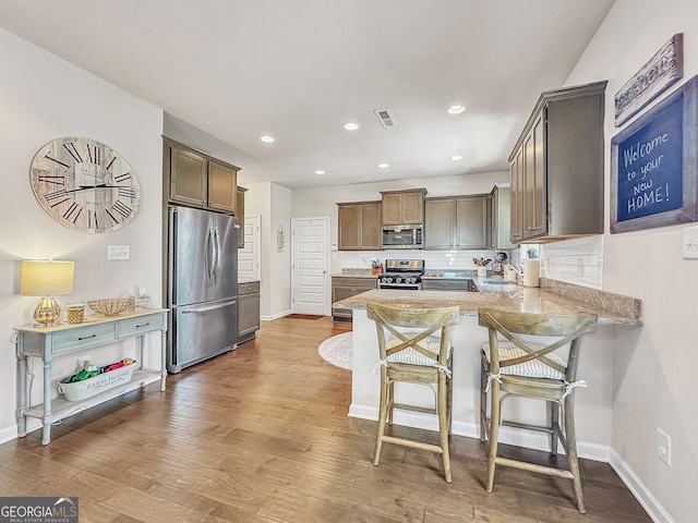 kitchen featuring tasteful backsplash, stainless steel appliances, wood-type flooring, kitchen peninsula, and a breakfast bar