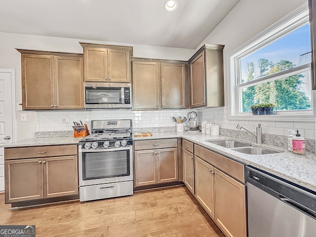 kitchen with light wood-type flooring, appliances with stainless steel finishes, light stone counters, sink, and decorative backsplash