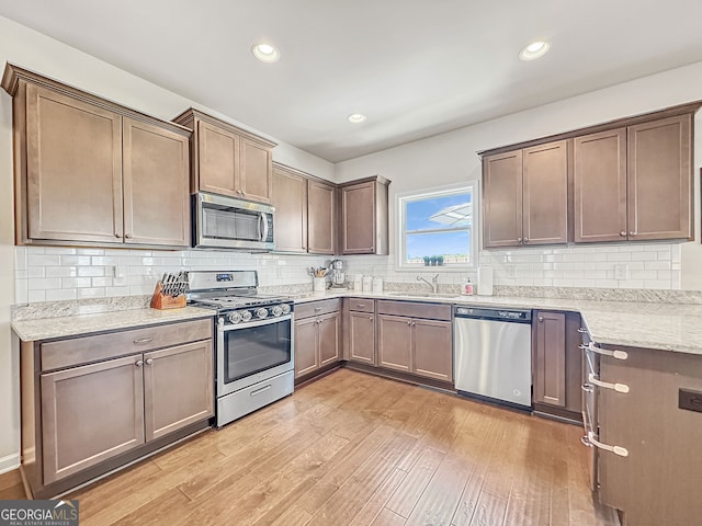 kitchen with tasteful backsplash, stainless steel appliances, sink, light stone countertops, and light hardwood / wood-style floors