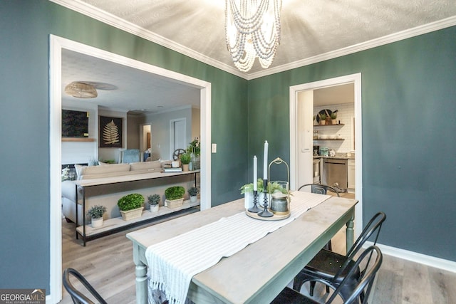 dining area featuring light wood-style floors, a chandelier, crown molding, and baseboards