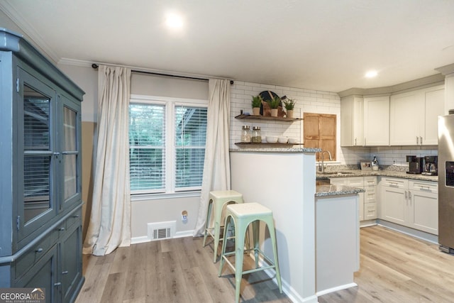 kitchen featuring light stone countertops, stainless steel fridge with ice dispenser, tasteful backsplash, light wood-type flooring, and white cabinets