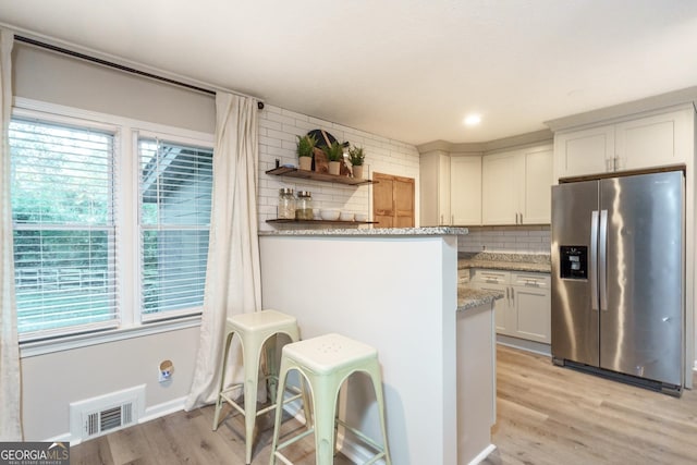 kitchen with light stone countertops, backsplash, white cabinetry, and stainless steel refrigerator with ice dispenser