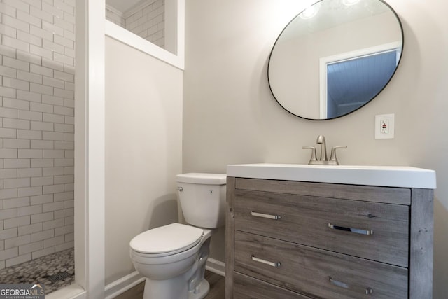 full bath featuring toilet, baseboards, tiled shower, and vanity