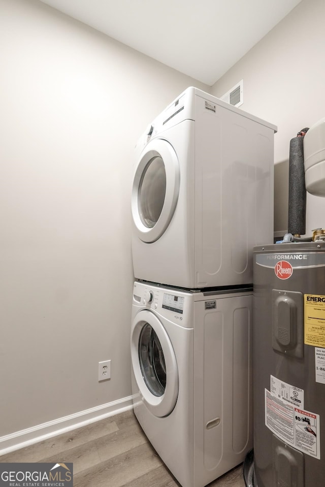 washroom featuring electric water heater, light wood-type flooring, and stacked washer and clothes dryer