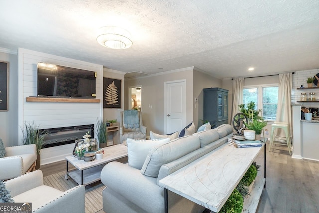 living room featuring a textured ceiling, wood finished floors, baseboards, ornamental molding, and a glass covered fireplace