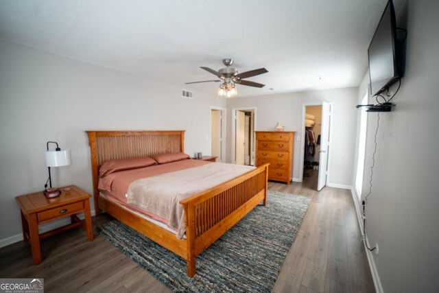 bedroom with wood-type flooring, a closet, a walk in closet, and ceiling fan