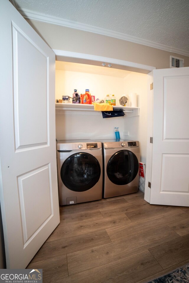 washroom with a textured ceiling, crown molding, washing machine and dryer, and dark hardwood / wood-style flooring