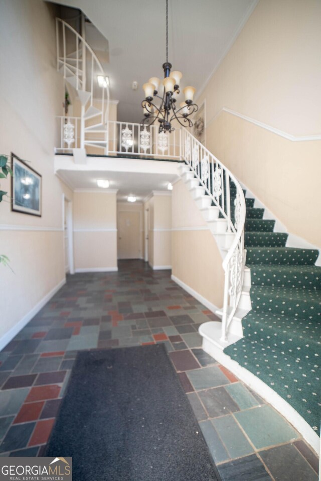 entryway with a towering ceiling, a chandelier, and crown molding