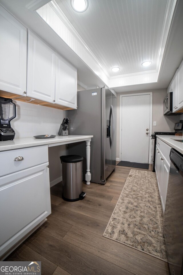 kitchen with white cabinetry, a tray ceiling, appliances with stainless steel finishes, dark hardwood / wood-style flooring, and decorative backsplash