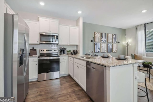 kitchen with stainless steel appliances, dark wood-type flooring, light stone counters, a breakfast bar, and white cabinetry