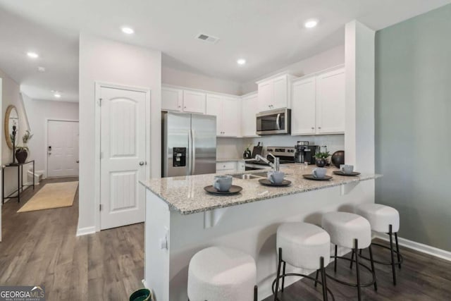 kitchen featuring white cabinetry, appliances with stainless steel finishes, a kitchen breakfast bar, light stone countertops, and dark hardwood / wood-style flooring