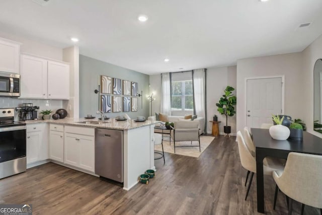 kitchen with dark wood-type flooring, white cabinetry, appliances with stainless steel finishes, and light stone counters