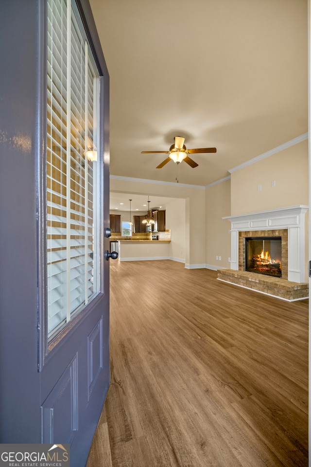 unfurnished living room with hardwood / wood-style floors, ceiling fan, crown molding, and a brick fireplace