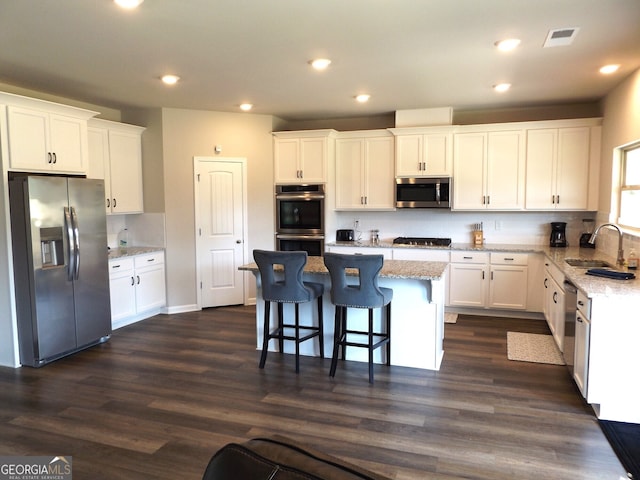 kitchen with stainless steel appliances, white cabinetry, sink, dark wood-type flooring, and a kitchen island