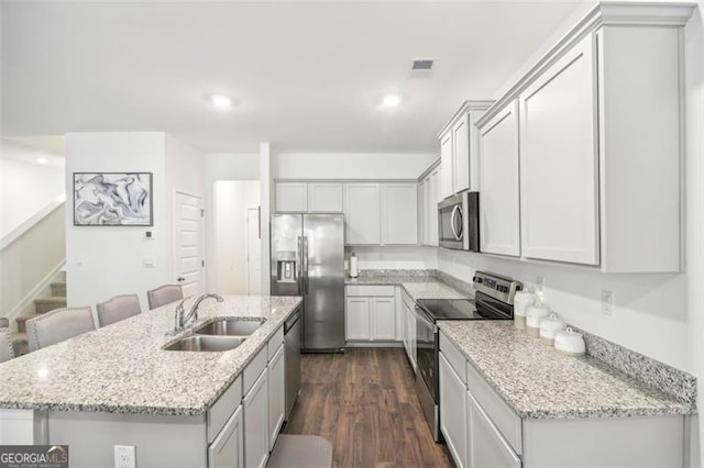 kitchen featuring a kitchen island with sink, dark wood-type flooring, a sink, visible vents, and appliances with stainless steel finishes