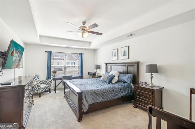 bedroom featuring light carpet, visible vents, a tray ceiling, and ceiling fan