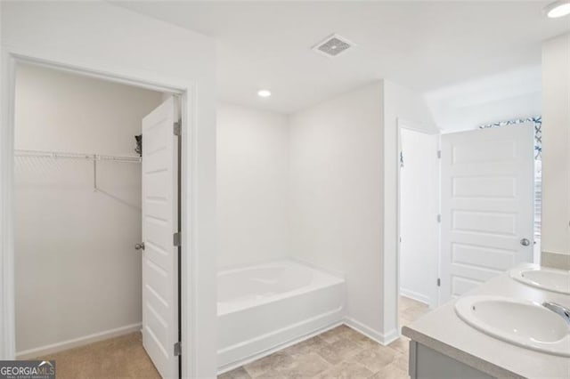 full bathroom featuring a sink, visible vents, baseboards, a bath, and a walk in closet