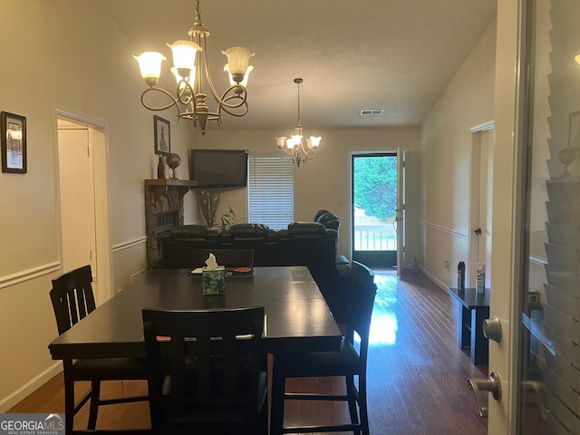 dining area with a textured ceiling, dark hardwood / wood-style floors, an inviting chandelier, a stone fireplace, and lofted ceiling