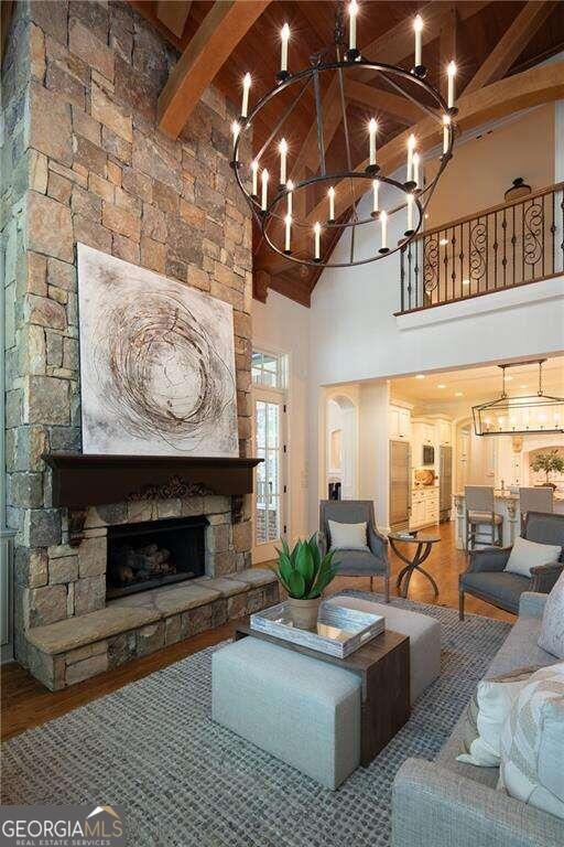 living room featuring high vaulted ceiling, a chandelier, wood-type flooring, and a stone fireplace