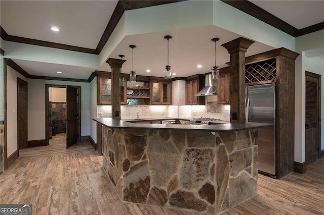 kitchen with wall chimney range hood, tasteful backsplash, ornate columns, and light hardwood / wood-style floors