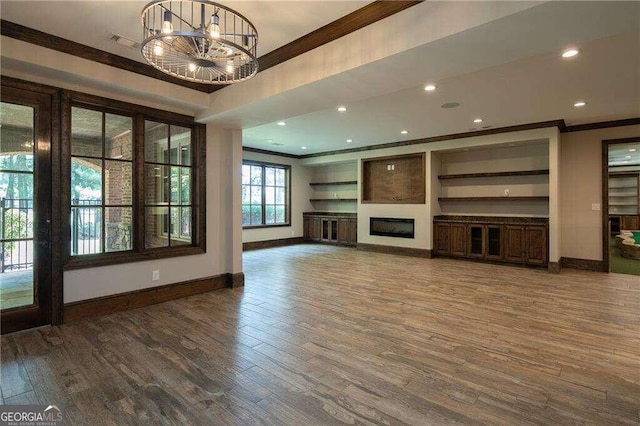 unfurnished living room featuring crown molding, wood-type flooring, and an inviting chandelier