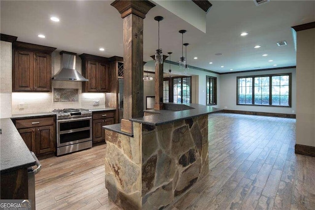 kitchen featuring light hardwood / wood-style flooring, range with two ovens, wall chimney range hood, and decorative backsplash