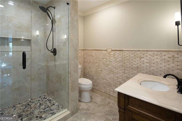 bathroom featuring vanity, a shower with shower door, tile walls, toilet, and ornamental molding