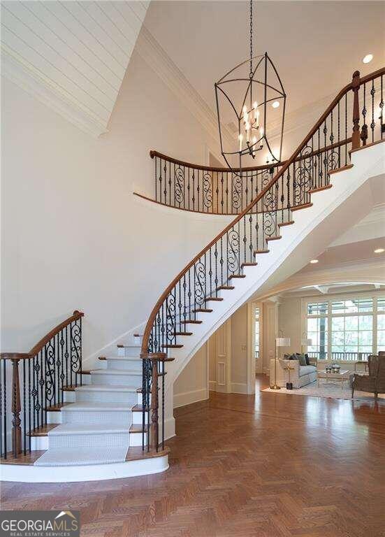 stairs with crown molding, a towering ceiling, parquet floors, and a notable chandelier