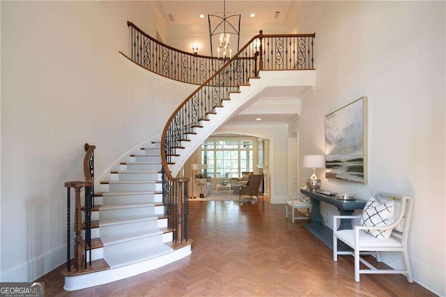 foyer entrance featuring a towering ceiling, ornamental molding, parquet flooring, and a chandelier