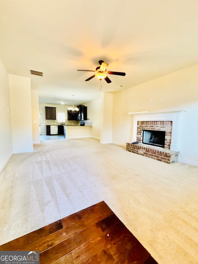 unfurnished living room featuring a brick fireplace, carpet floors, and ceiling fan