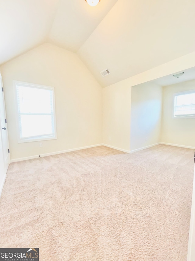 additional living space featuring vaulted ceiling and light colored carpet