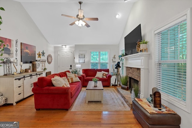 living room with high vaulted ceiling, ceiling fan, a brick fireplace, and light hardwood / wood-style flooring