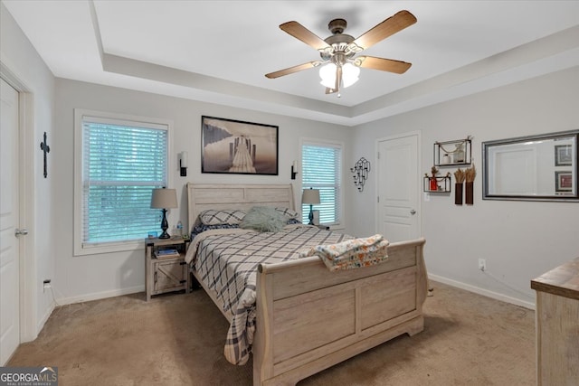 bedroom with ceiling fan, carpet floors, and a tray ceiling