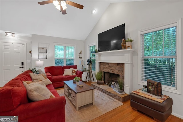 living room with ceiling fan, hardwood / wood-style floors, a stone fireplace, and high vaulted ceiling