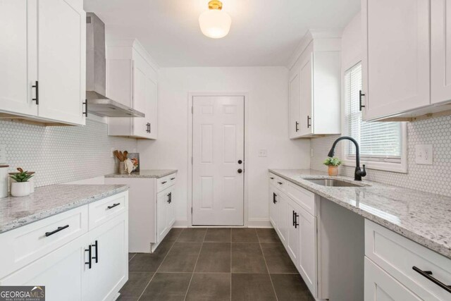 kitchen with dark tile patterned flooring, backsplash, sink, white cabinets, and wall chimney range hood