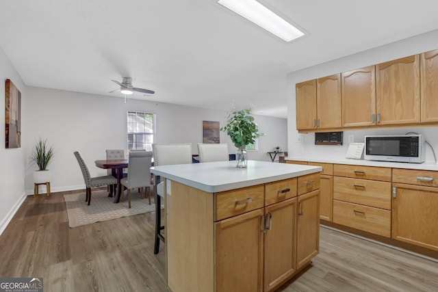 kitchen with light wood-type flooring, a breakfast bar area, a center island, and ceiling fan