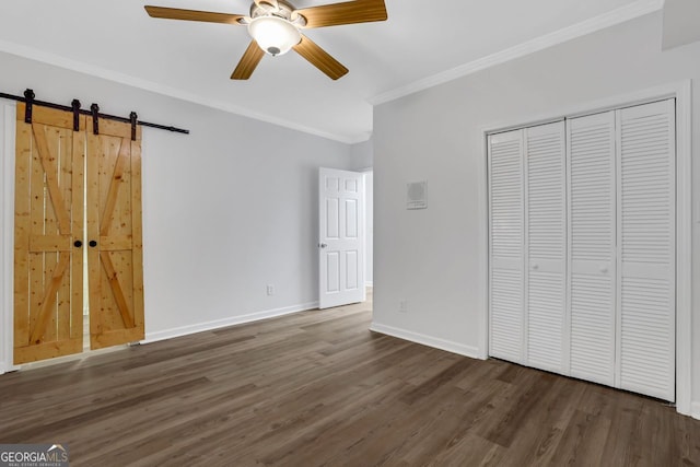 unfurnished bedroom with ceiling fan, crown molding, dark wood-type flooring, and a barn door