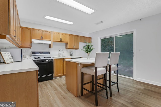 kitchen featuring gas stove, light hardwood / wood-style floors, sink, a kitchen island, and a kitchen breakfast bar